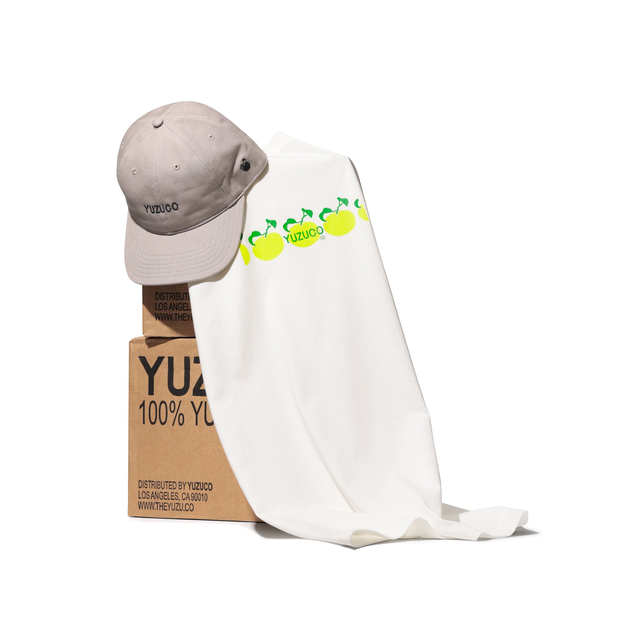 YUZUCO hat and tee shirt draped over brown cardboard custom YUZUCO juice cases